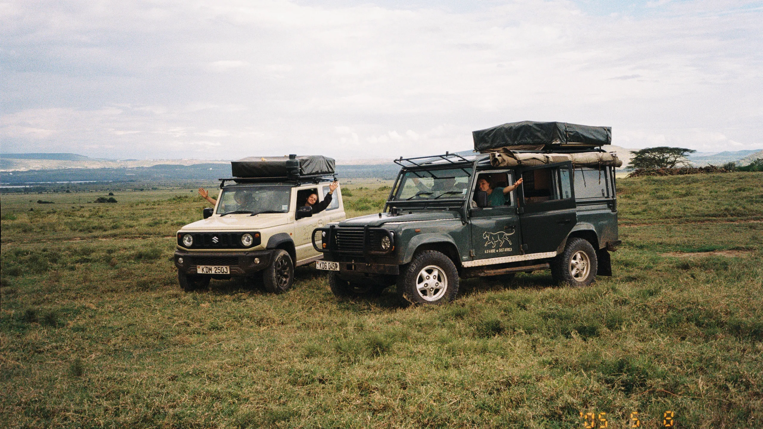 A Land Rover Defender and a Suzuki Jimny with rooftop tents parked on the Kenyan grassland, shot on film