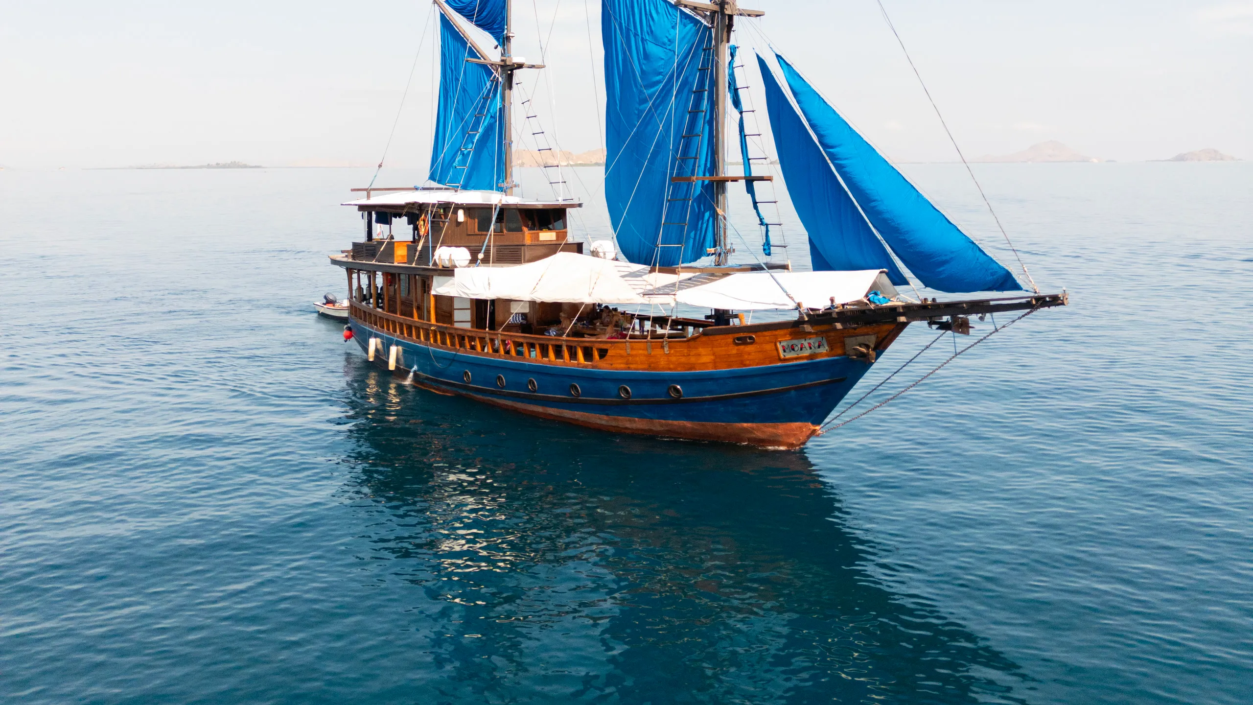 A traditional wooden sailing boat with blue sails on calm water in the Komodo Islands