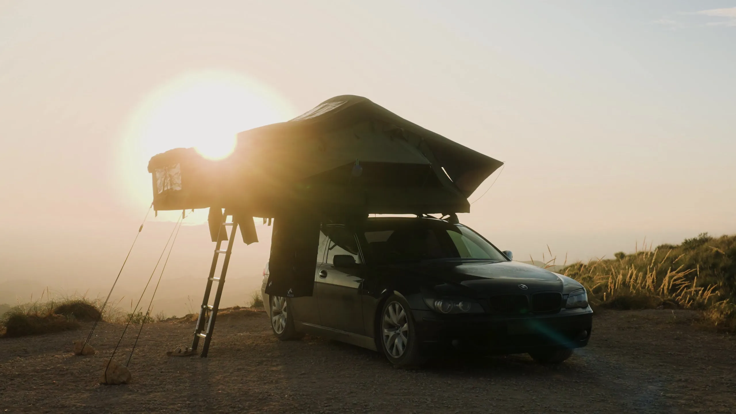 An Arcta rooftop tent on a car at sunrise, with the sun flaring behind it